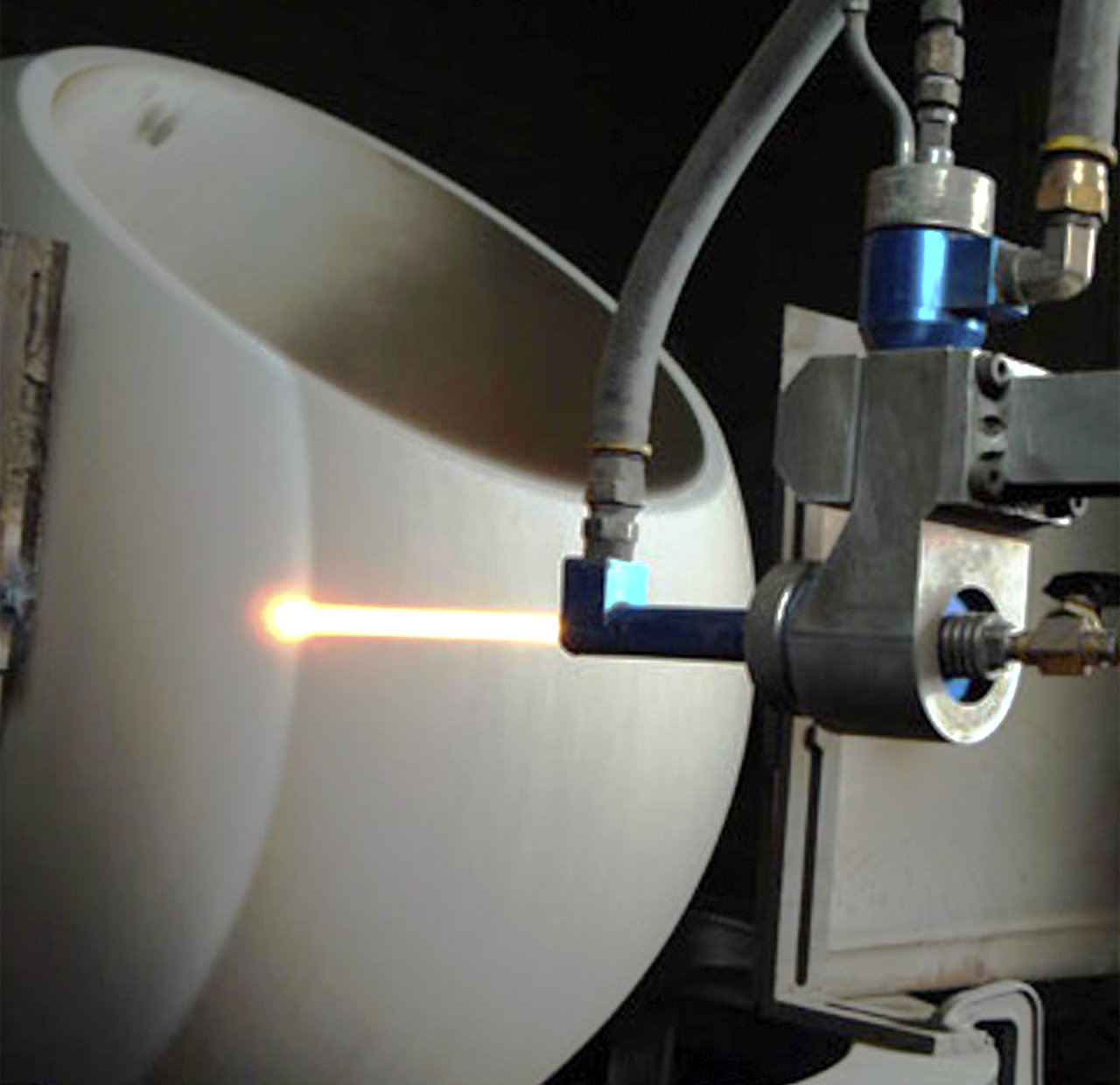 A robotic arm applies a high-heat laser to the surface of a large, cylindrical ceramic object, likely for manufacturing or repair purposes. The lighting focuses on the laser point, highlighting the precision of the robotic mechanism.